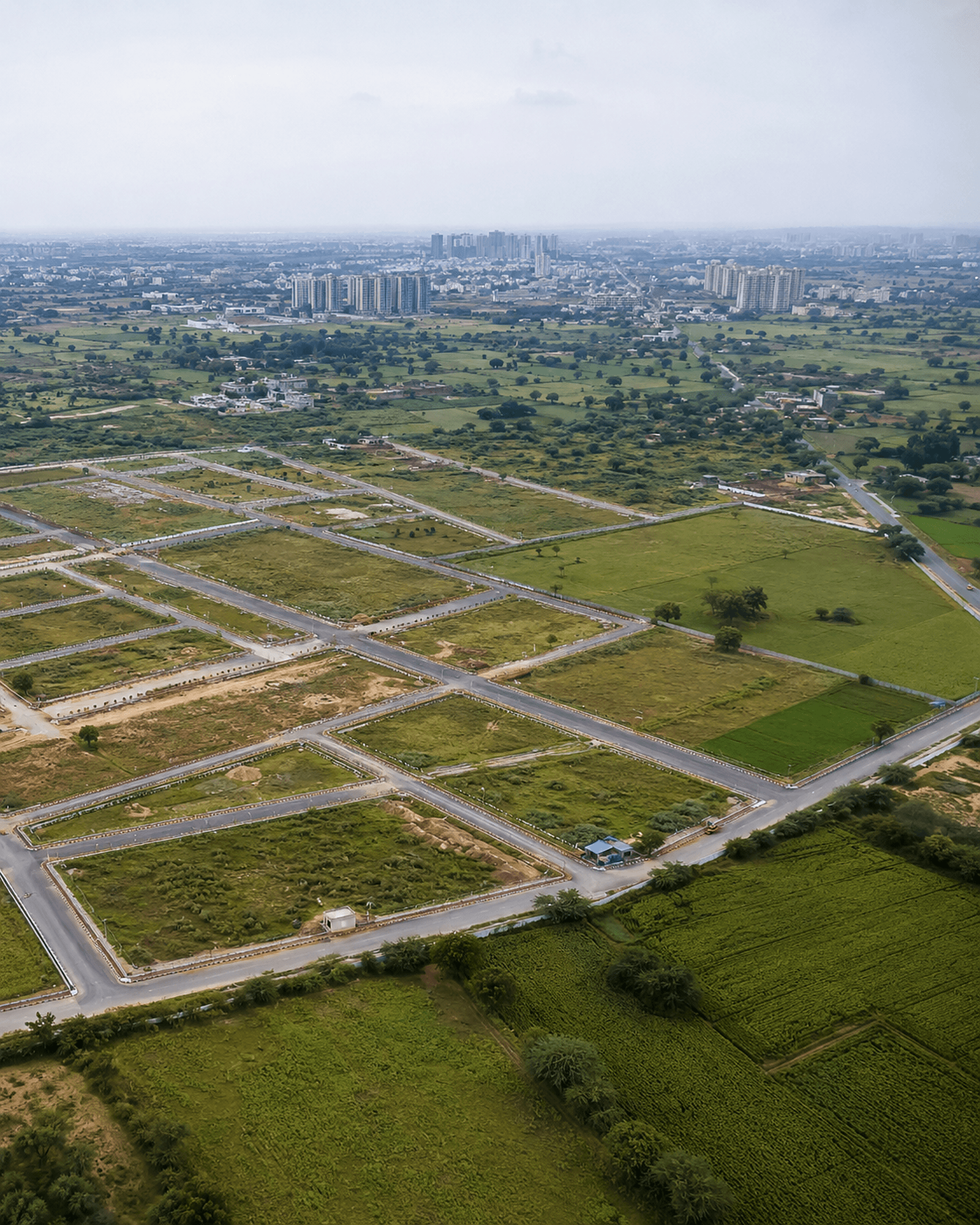 Aerial view of plotted, serviced land parcels laid out with road grids beside greenery — land development opportunities.