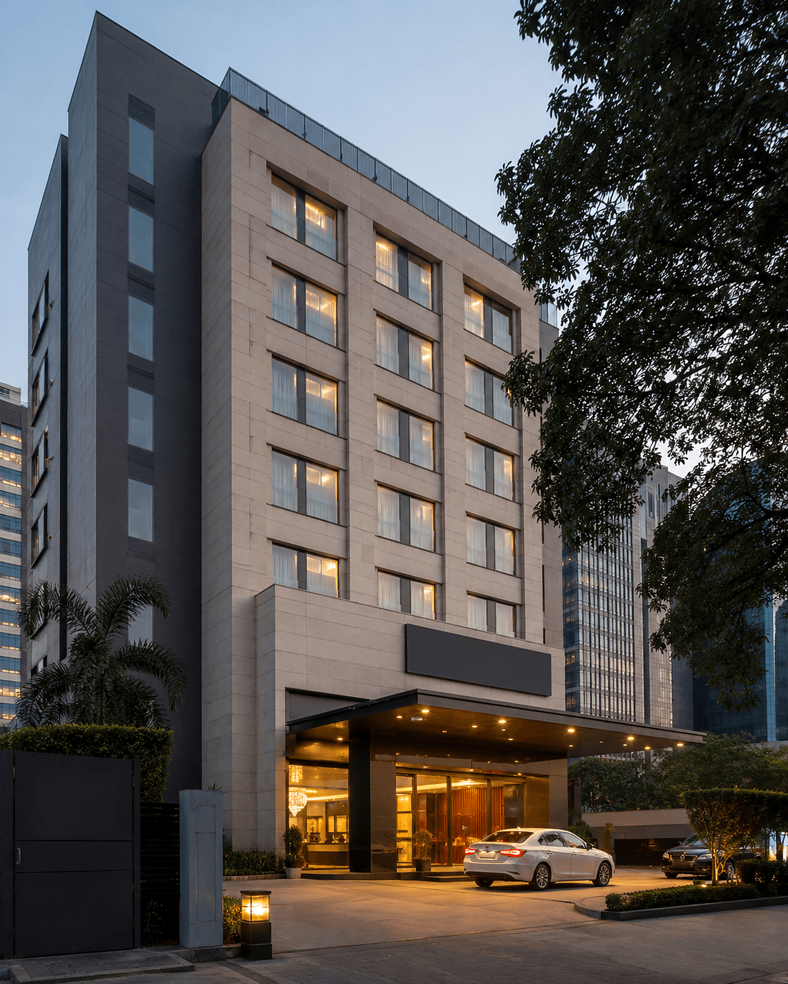 Compact business hotel with a lit porte-cochère and arrival drive at dusk — hospitality development.