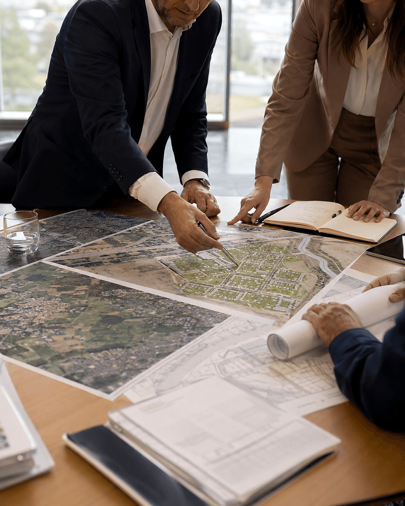 Partners reviewing aerial site maps and development plans across a boardroom table — joint development projects.